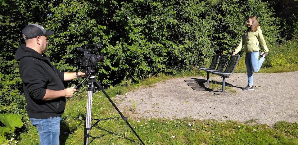 Mies kuvaa videokameralla venyttelevää naista puistossa.