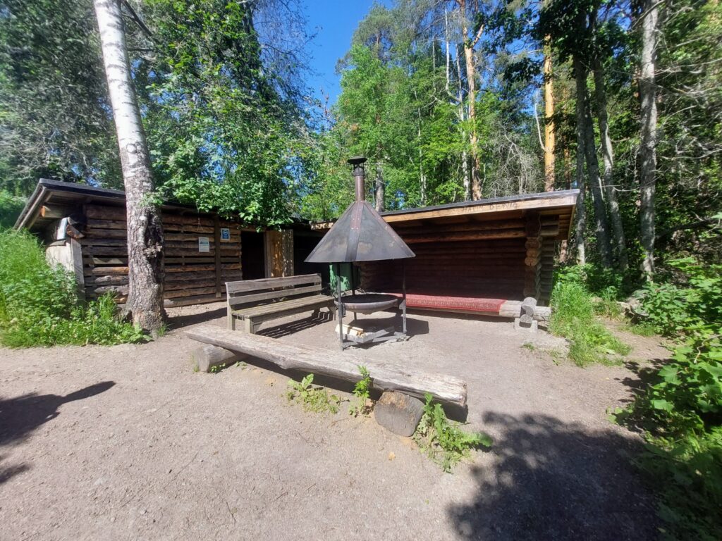 Hirsilaavu, edessä nuotiopaikka, taustalla metsää.