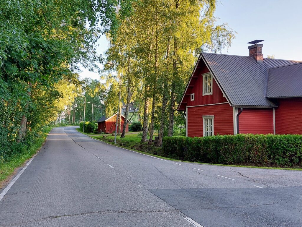 Maantie, oikealla punainen puutalo, puita